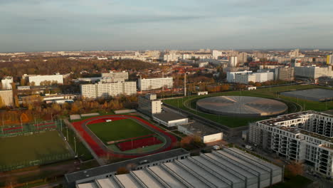 Red-Running-Track-sports-field-in-Urban-City-Area-with-futuristic-Velodrome-Building-cycling-Arena-in-Berlin,-Germany,-Aerial-slide-dolly-left-at-Sunset
