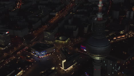 Close-up-Shot-of-Berlin-TV-Tower-Skyscraper-at-Night-with-German-Cityscape-in-distance,-Aerial-establishing-Shot