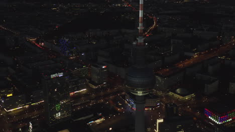 Close-up-View-of-Berlin-TV-Tower-Skyscraper-at-Night-with-German-Cityscape-in-distance,-Aerial-establisher