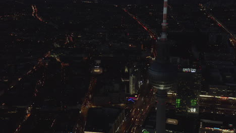 Flashing-City-lights-at-Night-with-TV-Tower-Skyscraper-in-foreground,-Aerial-Drone-Cityscape
