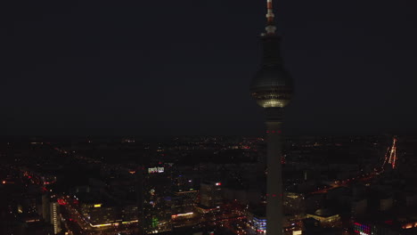 Skyscraper-Tower-Building-with-wide-Cityscape-at-Night-in-Background-with-glowing-lights-and-buildings-in-Berlin,-Germany-in-2019