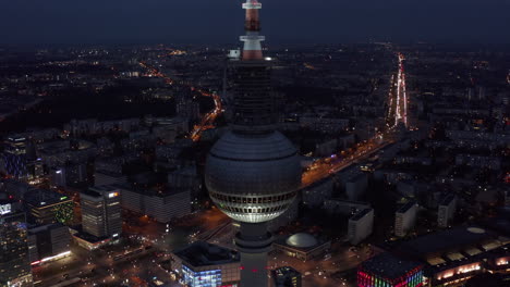 Berlin-tall-TV-Tower-at-Night-blinking-red-light-with-Cityscape-and-road-into-distance-in-the-background-in-Germany,-Aerial-Wide-Angle-Drone-View