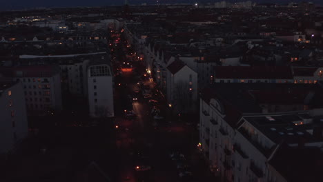 Forwards-tracking-car-driving-on-road-in-residential-neighbourhood.-Aerial-view-of-wide-street-with-parked-cars-after-sunset.-Berlin,-Germany.