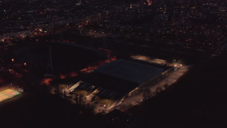 Flight-around-sports-areal,-modern-hall-and-football-stadium.-Aerial-footage-of-town-at-night.-Berlin,-Germany.