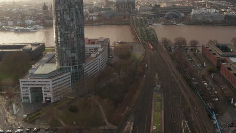 Aerial-footage-of-trains-driving-at-steel-railway-bridge-over-Rhine-river-at-golden-hour.-Cologne,-Germany