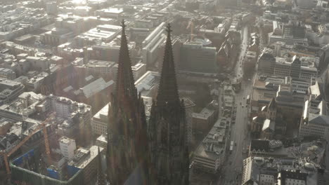 Aerial-slide-and-pan-shot-of-pair-of-towers-of-gothic-Cathedral-Church-of-Saint-Peter.-Sunshine-reflecting-by-wet-roofs-of-town-development.-Cologne,-Germany