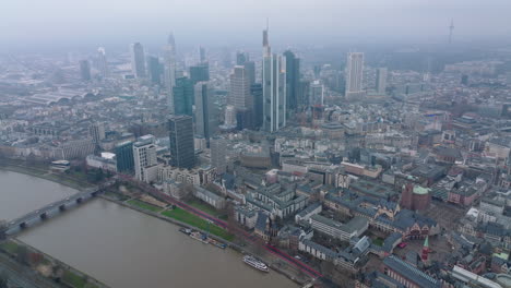 Aerial-panoramic-footage-of-city-with-high-rise-buildings-in-business-hub.-Hazy-view-of-large-town.-Wide-river-calmly-flowing.-Frankfurt-am-Main,-Germany