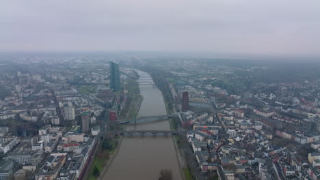 Forwards-fly-above-large-city.-Various-bridges-spanning-river.-Aerial-panoramic-hazy-view-of-urban-neighbourhoods.-Frankfurt-am-Main,-Germany