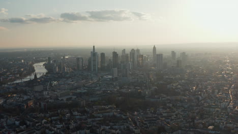 Aerial-view-of-tall-modern-buildings-downtown-from-slowly-backwards-flying-drone.-Cityscape-with-skyscrapers-against-bright-sky.-Frankfurt-am-Main,-Germany
