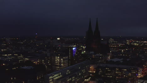 AERIAL:-Wide-Shot-of-Cologne-Germany-from-the-air-with-majestic-Cathedral-at-Night