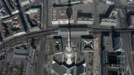 AERIAL:-Super-Close-Up-View-of-the-top-of-Alexanderplatz-TV-Tower-with-Berlin,-Germany-Streets-in-background-on-hot-summer-day
