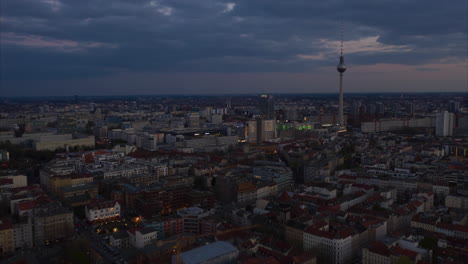 Backwards-fly-above-city-at-sunset-time.-Visible-dimming-light.-Hyperlapse-of-cityscape-with-Fernsehturm-TV-tower,-Berlin,-Germany