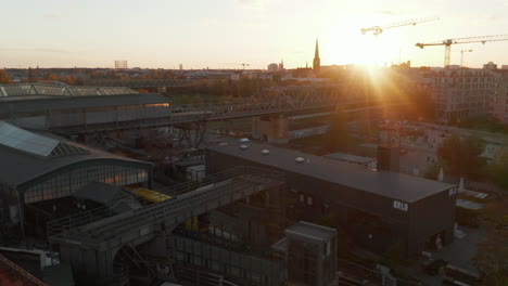 Scenic-Aerial-Shot-of-Yellow-Subway-Train-entering-Station-elevated-above-ground-in-Berlin,-Germany-at-Sunset
