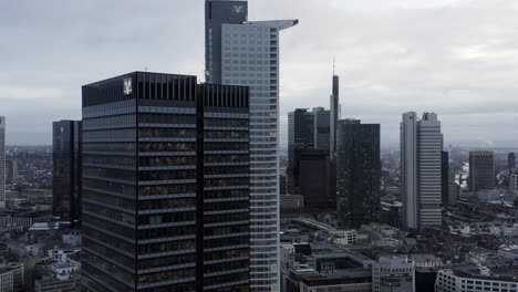 AERIAL:-Rising-up-along-Skyscraper-in-Frankfurt-am-Main,-Germany-on-Cloudy-Grey-Winter-Day-with-City-Traffic