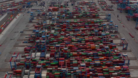 Aerial-view-of-rows-of-colorful-cargo-containers-in-large-industrial-port-being-moved-by-automated-cranes