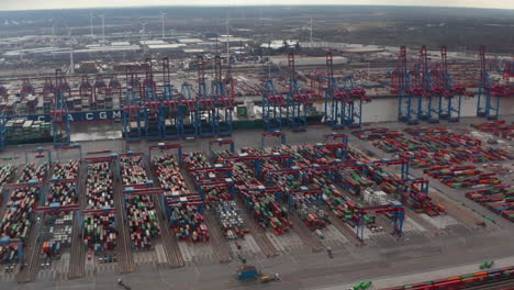 Aerial-view-of-cranes-and-wind-turbines-in-large-industrial-cargo-container-port-in-Hamburg,-Germany