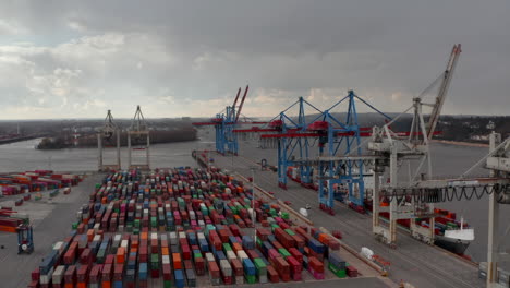 Slow-aerial-dolly-in-view-of-large-cargo-cranes-above-rows-of-colorful-containers-in-Hamburg-industrial-port