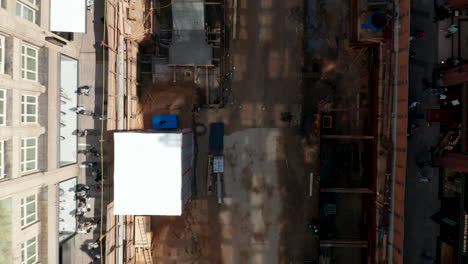Aerial-birds-eye-overhead-top-down-view-of-people-walking-along-construction-site-in-town-street.-Descending-view