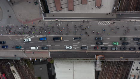 Aerial-birds-eye-overhead-top-down-view-of-group-of-cyclists-passing-by-queue-of-cars-on-bridge-across-railway.-Pride-parade-on-bikes-Free-and-Hanseatic-City-of-Hamburg,-Germany