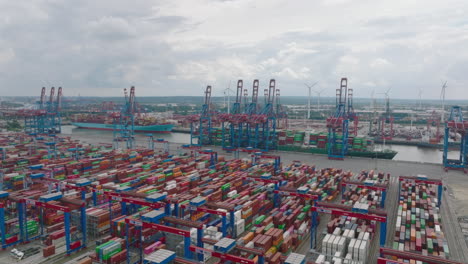 Fly-above-large-logistic-areal-in-harbour.-Thousand-of-containers-waiting-for-delivery-to-customer.-Heavy-cranes-loading-and-unloading-units-from-huge-overseas-cargo-ships.-Hamburg,-Germany