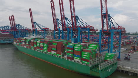 Majestic-cargo-ship-with-loaded-thousands-of-overseas-containers.-Ascending-footage-of-cargo-terminal-in-harbour.-Intermodal-transport-and-global-logistics.-Hamburg,-Germany