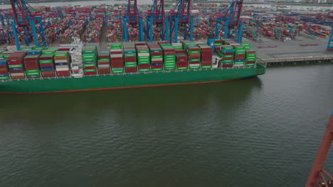 Forwards-fly-above-harbour.-Tilt-up-reveal-of-huge-cargo-ship-and-rows-of-colour-containers-in-logistic-terminal.-Intermodal-transport-and-global-logistics.-Hamburg,-Germany