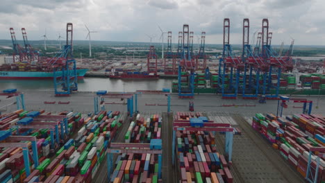 Slider-of-machinery-in-harbour-cargo-terminal.-Aerial-view-of-stacked-overseas-containers-and-majestic-gantry-cranes-loading-large-ships.-Intermodal-transport-and-global-logistics.-Hamburg,-Germany
