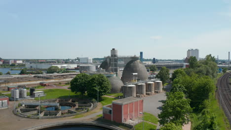 Landing-footage-of-bulbous-concrete-tanks-in-industrial-site-next-by-circle-sump-tanks-in-wastewater-treatment-plant.-Luebeck,-Schleswig-Holstein,-Germany