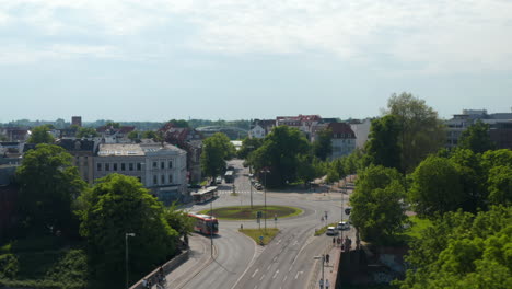 Forwards-reveal-of-roundabout.-Aerial-view-of-main-road-with-low-traffic-leading-through-town.--Luebeck,-Schleswig-Holstein,-Germany