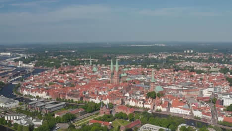 Aerial-panoramic-view-of-medieval-city-centre-lined-with-Trave-river.-Holsten-Gate,-St.-Marys,-St.-Peters-and-St.-Jacobs-churches.-Luebeck,-Schleswig-Holstein,-Germany