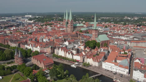 Forwards-fly-to-historic-brick-buildings-in-medieval-city-centre.-Aerial-view-of-Trave-river-waterfront-street-with-restaurant-terraces.-Luebeck,-Schleswig-Holstein,-Germany