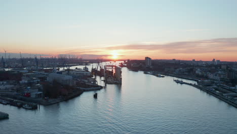 Warehouses-in-industrial-district-of-Hamburg-harbor-with-cargo-port-in-the-distance-during-sunset