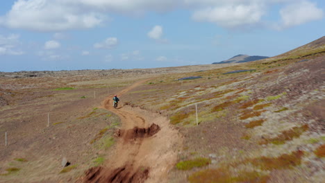 Aerial-view-following-man-doing-motocross-over-hill-on-Iceland.-Drone-view-of-biker-riding-on-dirt-road-among-mountains