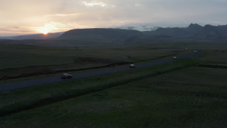 Drohnenflug-Aus-Der-Luft-über-Den-Abendlichen-Ringstraßenverkehr-In-Island.-Vogelperspektive-Von-Autos,-Die-Bei-Sonnenuntergang-Eine-Gerade-Straße-Durch-Das-Grasbewachsene-Hochlandtal-Hinunterfahren