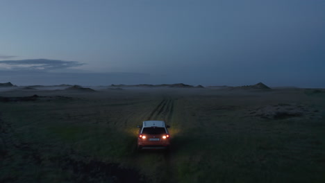 Aerial-view-flying-towards-adventurous-car-driving-on-wild-trail-in-Iceland-countryside.Commercial-aerial-view-of-tourist-travelling-greenland-in-Iceland-off-road-sightseeing-wilderness-at-night