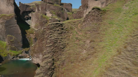 Vogelauge-Von-Grünen-Hügeln-Der-Schlucht,-Durch-Die-Ein-Fluss-In-Island-Fließt.-Luftaufnahme,-Die-Durch-Moosbedeckte-Hügel-Fliegt-Und-Die-Schlucht-In-Der-Isländischen-Landschaft-Entdeckt