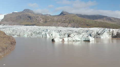 Aerial-panning-view-of-icebergs-swimming-in-the-Jokulsarlon-glacier-lake-in-Vatnajokull-National-Park,-Iceland.-Glacier-lagoon-with-big-ice-blocks,-melting-and-cracking-from-the-main-glacier