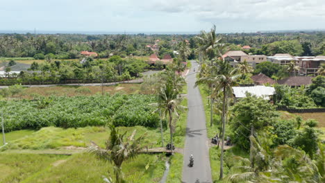 Aerial-dolly-shot-following-a-motorcyclist-driving-on-the-road-through-the-traditional-residential-neighborhood-in-Bali,-Indonesia