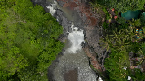 Top-down-overhead-aerial-view-of-a-jungle-river-with-waterfall-and-colorful-outdoor-restaurant-in-a-tropical-rainforest-of-Bali