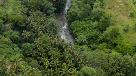 Aerial-tilting-shot-closing-in-on-the-jungle-river-flowing-across-stones-in-a-tropical-rainforest