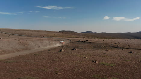 Aerial-view-drone-following-a-car-stirring-up-a-large-dust-cloud-as-it-speeds-along-desert-road.-Birds-eye-view-car-travelling-desert-path-discovering-uninhabited-parts-of-Iceland.-Freedom-concept