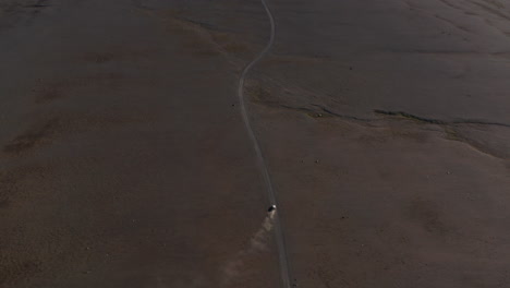Top-down-view-4x4-vehicle-driving-highway-in-remote-dusty-desert-in-icelandic-countryside.-Overhead-view-of-iceland-highlands-with-rocky-desert-and-off-road-car-driving-loneliness-motorway