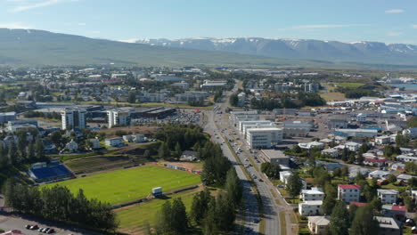 Aerial-footage-of-multilane-road-leading-through-urban-neighbourhood.-Snow-capped-mountains-in-background.-Akureyri,-Iceland