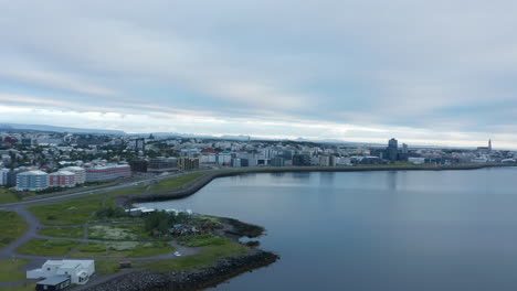 Elevated-panoramic-footage-of-city.-Road-leading-on-coast-and-various-buildings-in-urban-neighbourhood.-Calm-water-surface.-Reykjavik,-Iceland