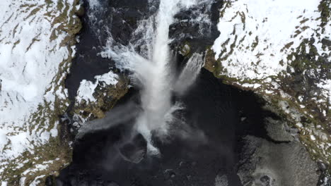 AERIAL:-Close-Up-of-Waterfall-in-Snow,-Ice-Canyon-in-Iceland-Green-Grass,-Cloudy