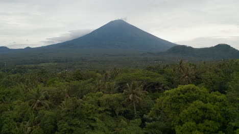 Slow-aerial-shot-of-rainforest-at-the-foot-of-mountain-Agung-in-Bali.-Large-tall-Mount-Agung-peak-rising-above-the-jungle-in-Indonesia