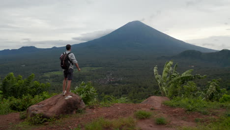 Tourist-observing-Mount-Agung-in-Bali-next-to-two-motorcycles.-Man-looking-at-large-mountain-peak-rising-above-the-jungle-in-Indonesia-from-the-tourist-observation-point