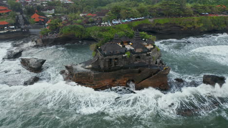 Overhead-aerial-rotating-view-of-stunning-buildings-in-Tanah-Lot-temple-on-a-dark-ocean-cliff-in-rough-sea-in-Bali,-Indonesia
