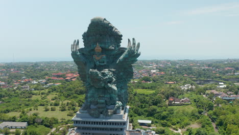Circling-a-majestic-Garuda-Wisnu-Kencana-statue-in-Bali,-Indonesia.-Huge-religious-monument-sculpture-of-Vishnu-riding-Garuda-rising-above-the-city