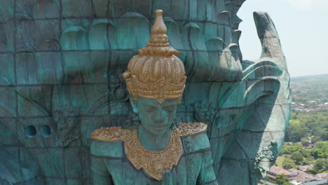 Face-of-Hindu-deity-Vishnu-in-Garuda-Wisnu-Kencana-statue-in-Bali,-Indonesia.-Close-up-aerial-view-of-religious-figure-on-large-copper-statue-rising-above-the-city